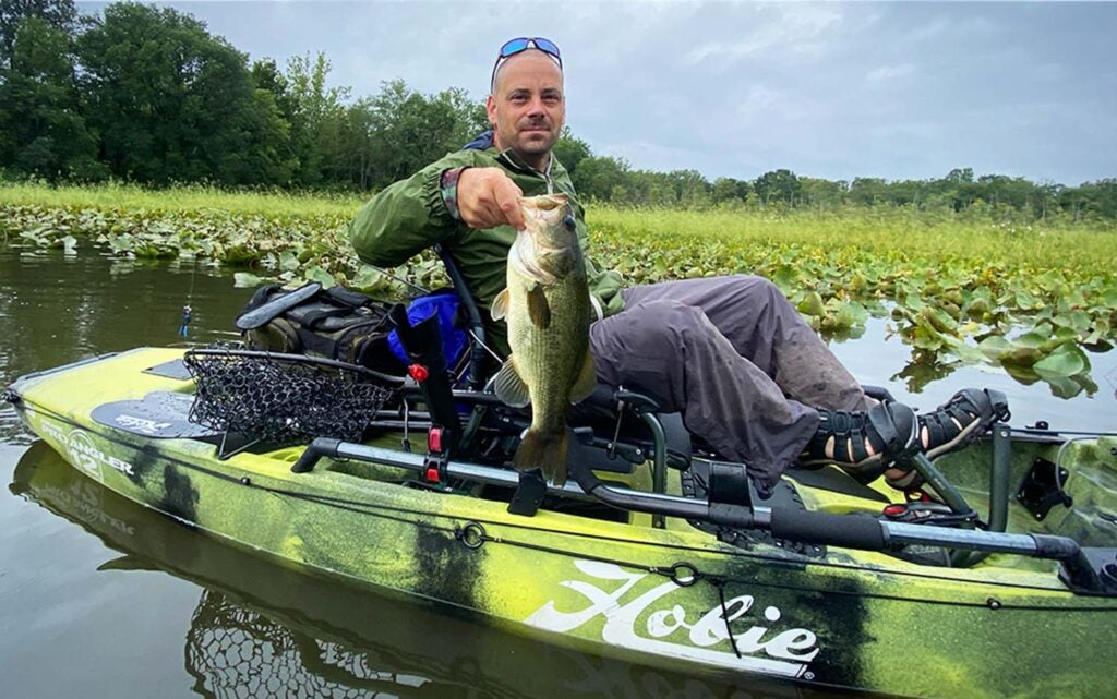 A man in a fishing kayak holding a fish and a best kayak fishing net