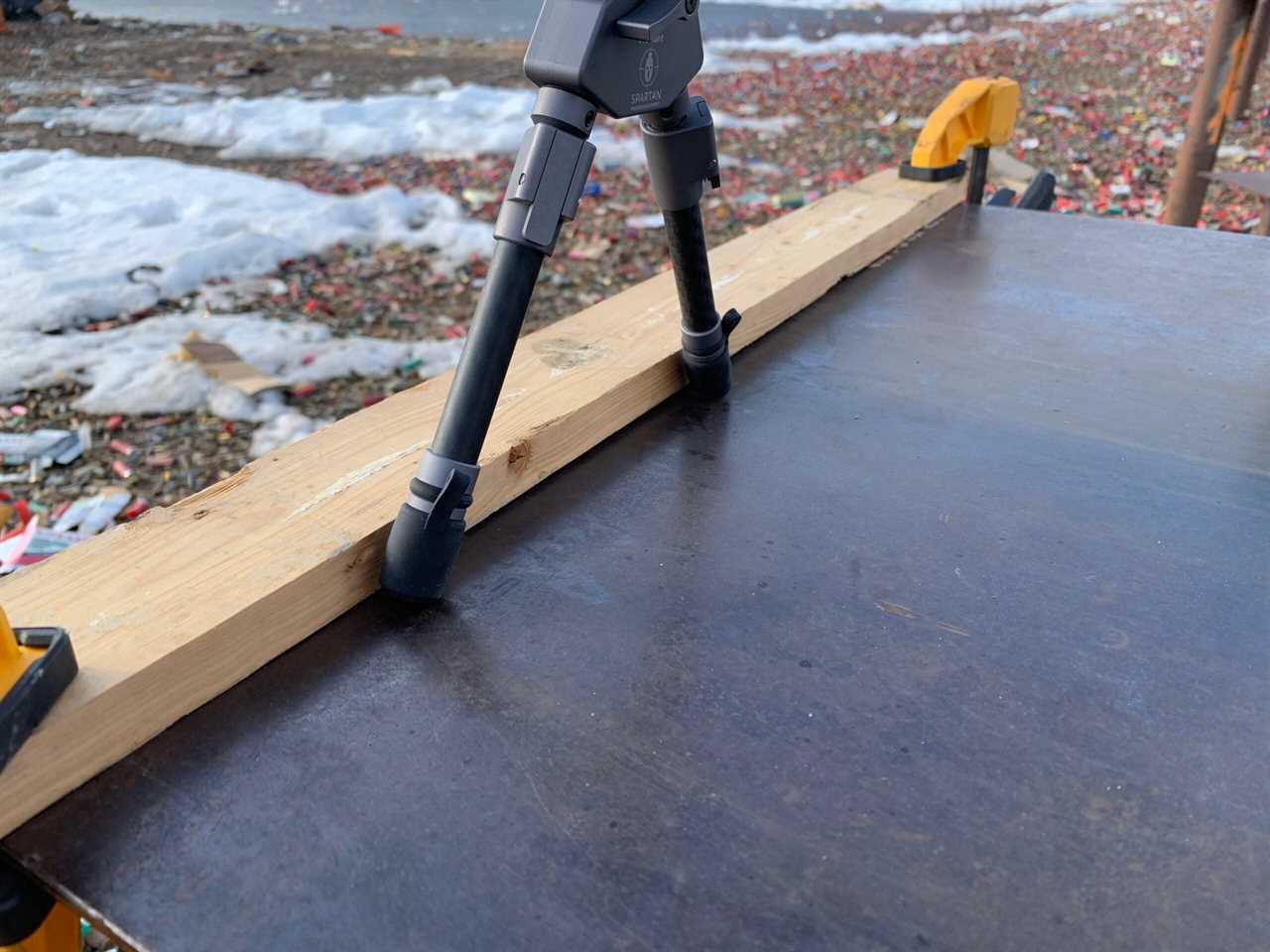 A board clamped to a shooting bench to load the bipod against