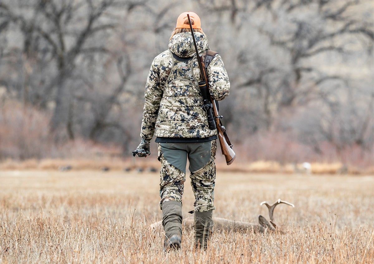 Hunter wearing SITKA women's timberline pants approaches buck.