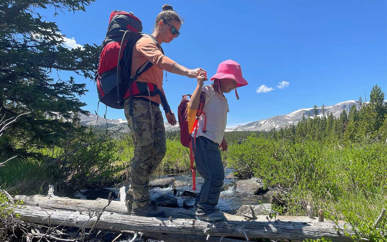 Woman wearing KUIU Women's Attack Pant helps daughter across a log.