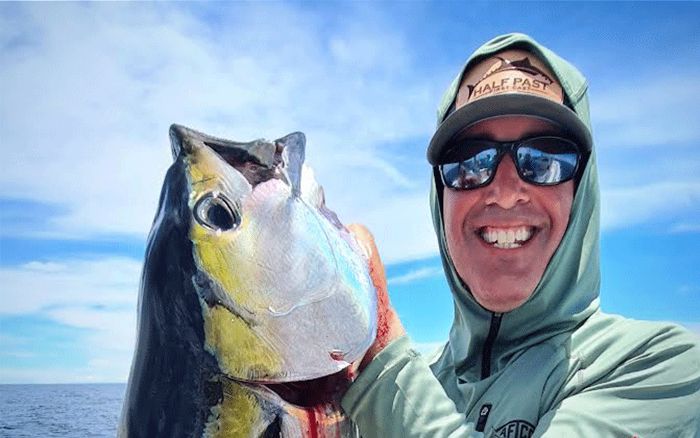 A man holding a fish wearing a hat and blue-lens sunglasses