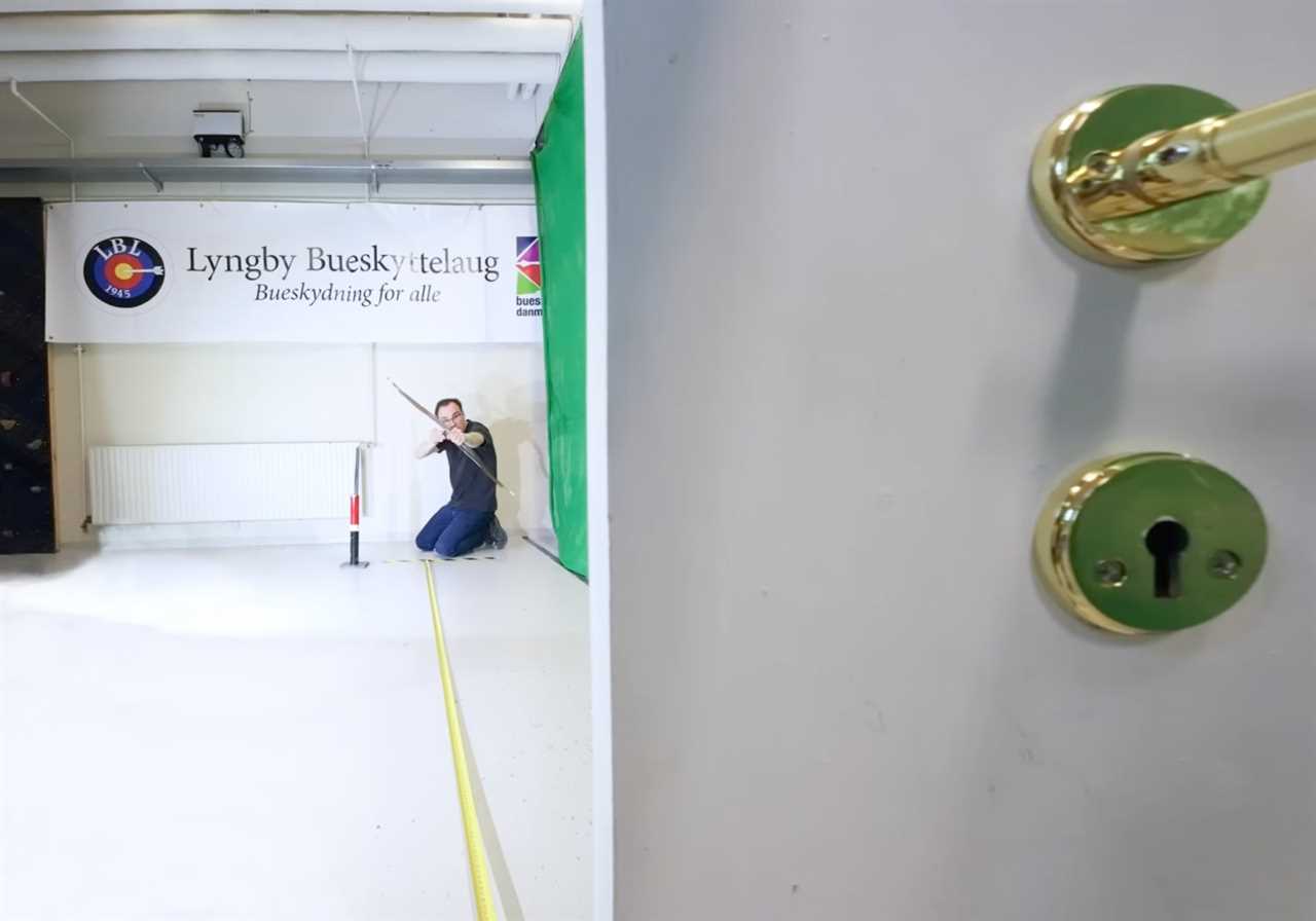 Lars Andersen draws to shoot an arrow through a keyhole.