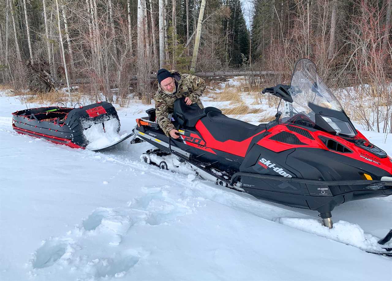 A hunter adjusts something on a red snow machine.