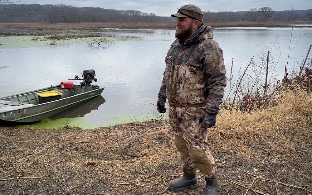 A man standing on the bank of a lake in waders