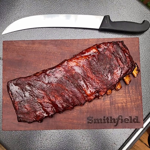 Smoked spare ribs with a large Cimeter style knife on a wood cutting board