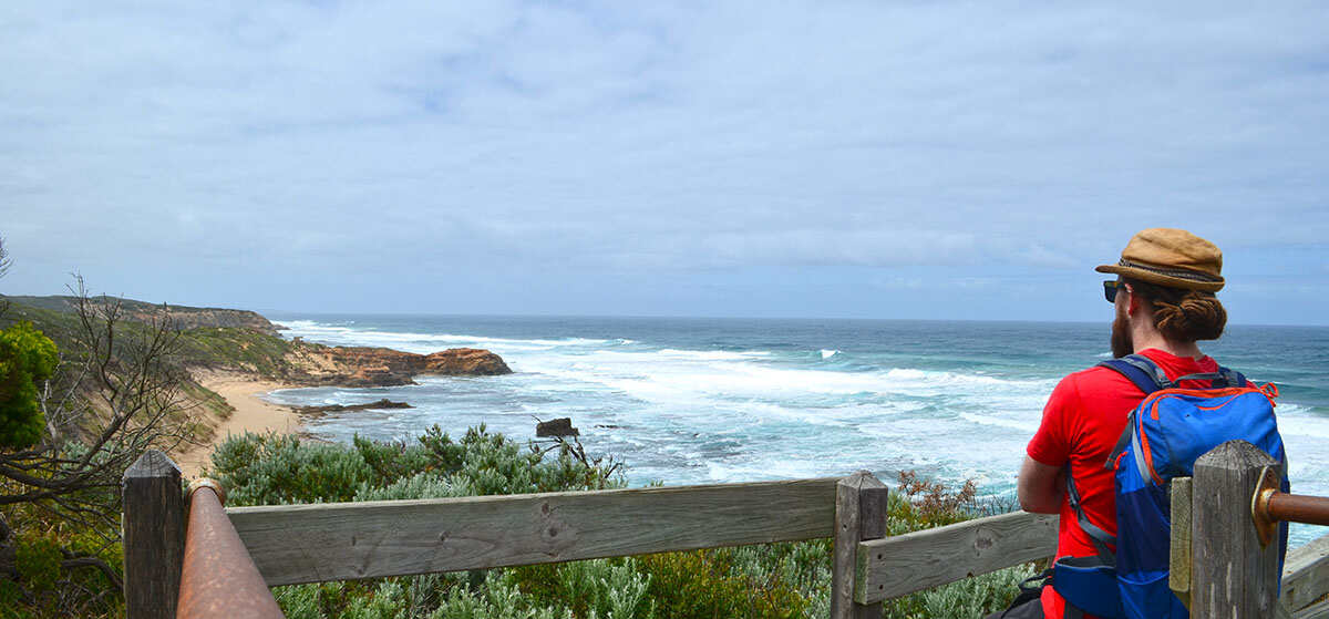 Neil checking out the bay views at Point Nepean National Park, leaning against the wooden rails at the top of a beach staircase
