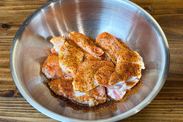 raw wings with seasoning sprinkled on top in a metal bowl