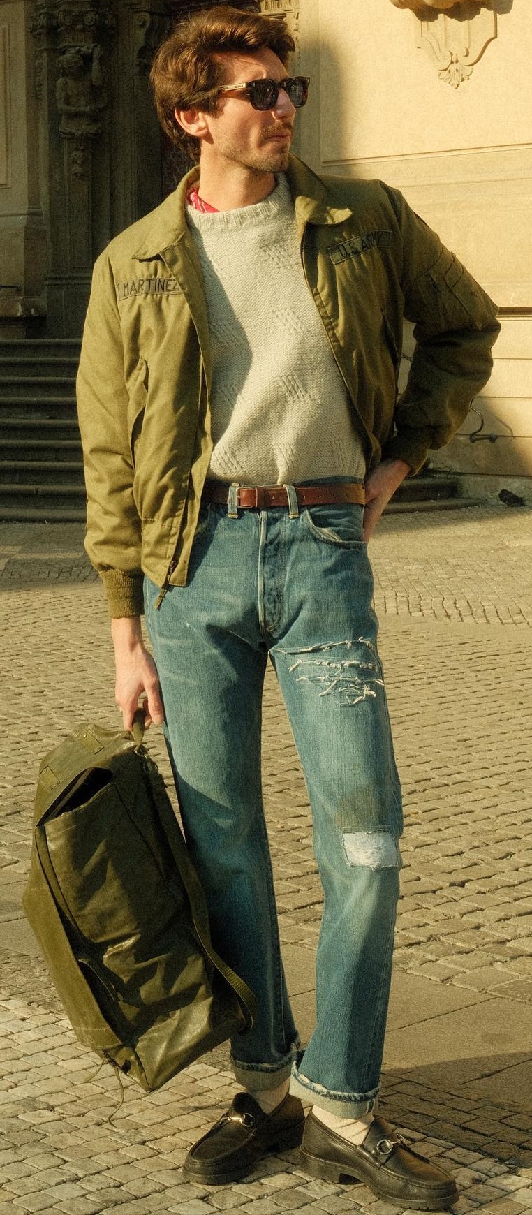 Gucci loafers being a must-have product with ripped denim and cream colored tshirt with a green jacket, accessorized with shades and a bag