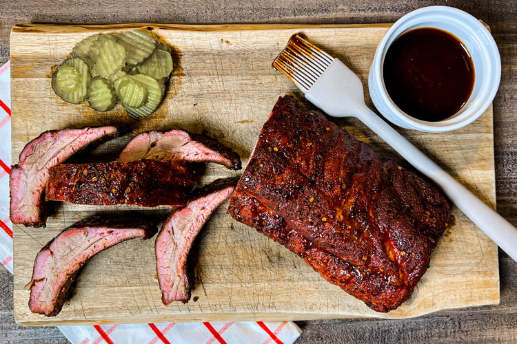 no wrap ribs plated on a wooden board with pickles, sauce and a basting brush