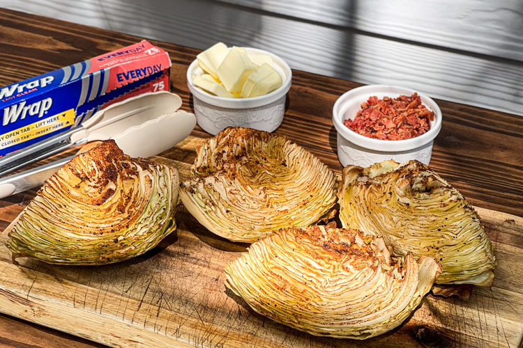 cooked cabbage quarters on a wooden chopping board before foil wrap