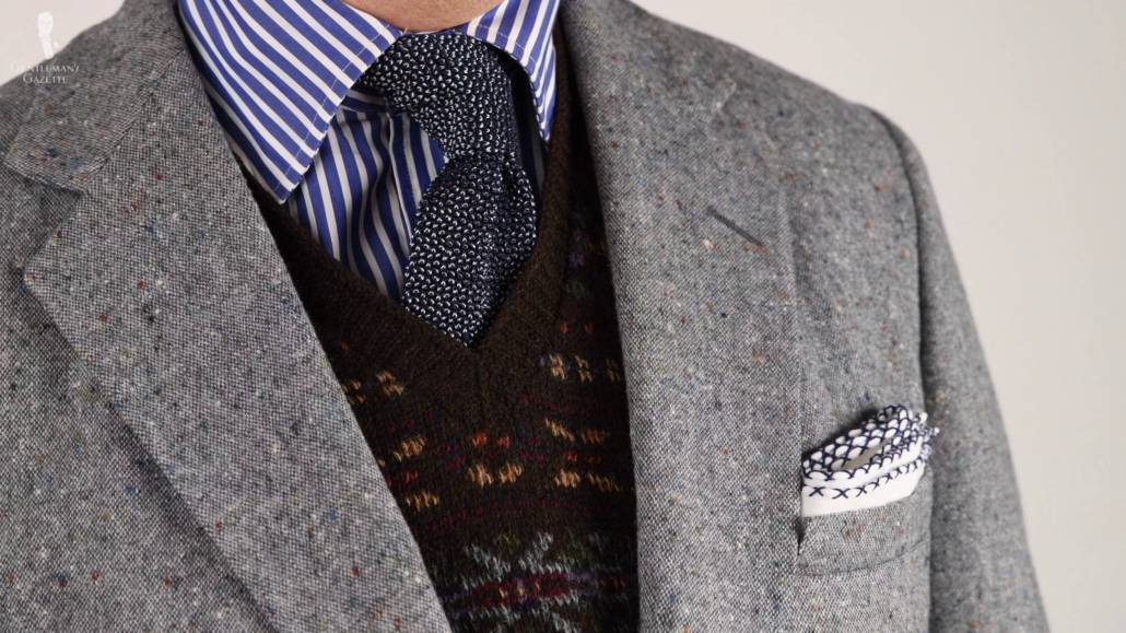 Gray Donegal jacket with a Fair Isle sweater, a blue shirt with white stripes, and a white linen pocket square with blue cross stitches along the edges and a dark blue and light blue two tone silk knit tie.