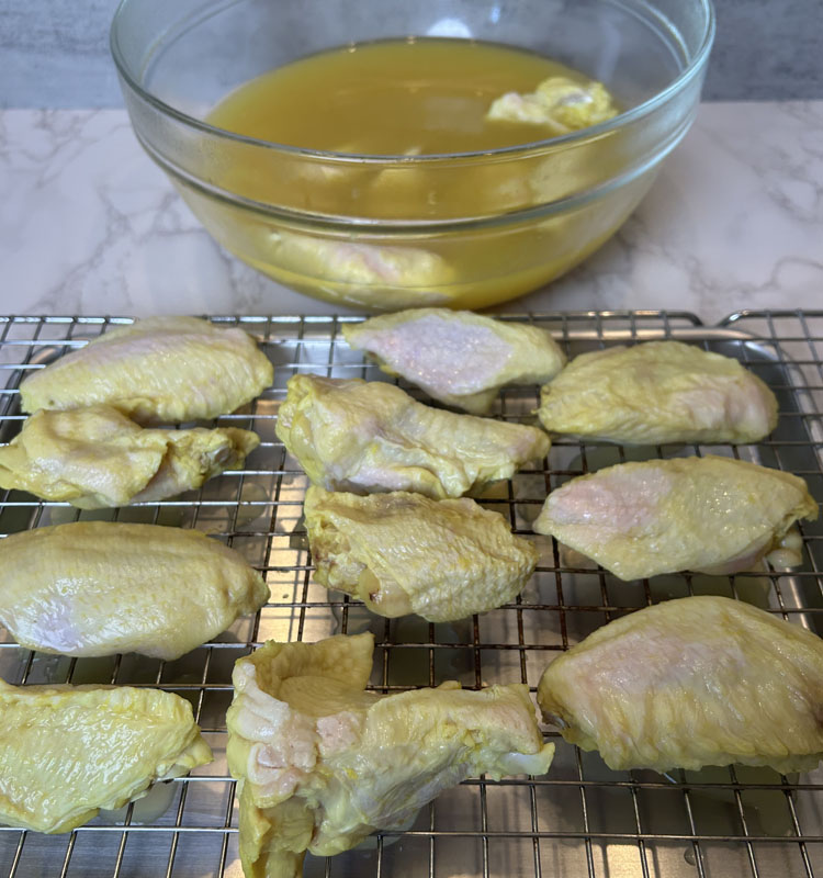 wings on a wire rack with a bowl of marinating wings in the background