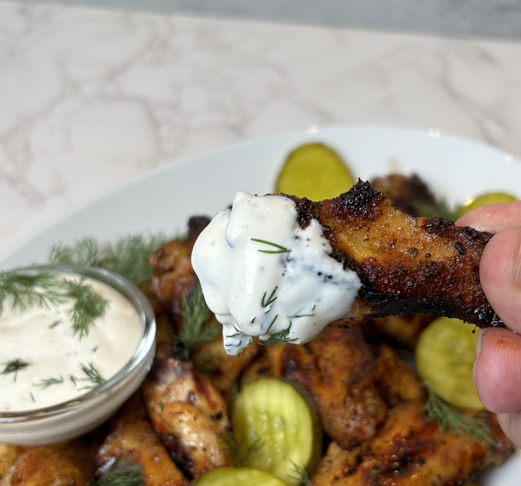 a pickleback wing dipped in dressing being held by fingers