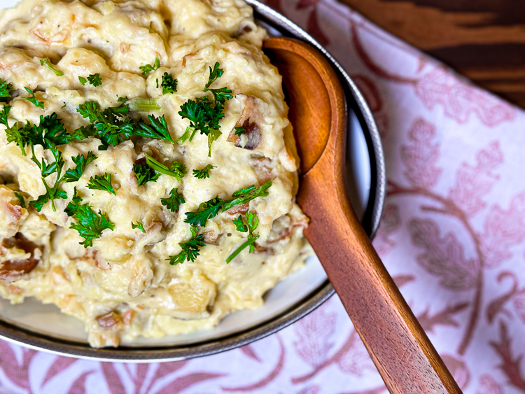 a serving bowl with smoked garlic mashed potatoes and a wooden spoon