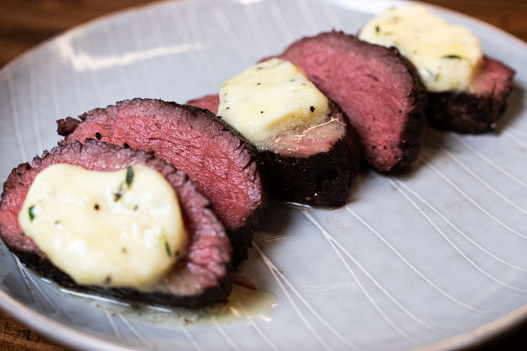 sliced reverse seared teres major steak with slice of compound butter