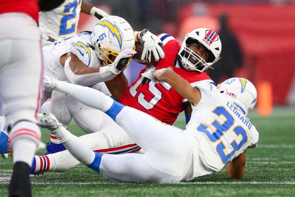 Ezekiel Elliott #15 of the New England Patriots runs with the ball while being tackled by Eric Kendricks #6 and Deane Leonard #33 of the Los Angeles Chargers in the third quarter at Gillette Stadium on December 03, 2023 in Foxborough, Massachusetts.