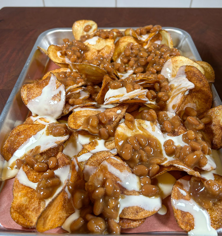 chips on a metal tray with queso and baked beans