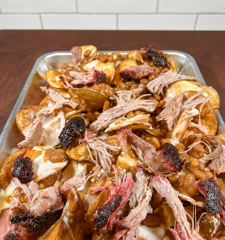 chips on a metal tray with queso, baked beans and pulled pork