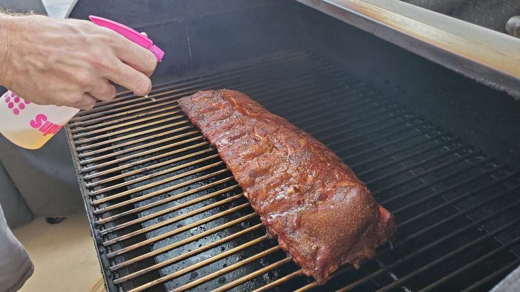 Spritzing baby back ribs on a pellet grill