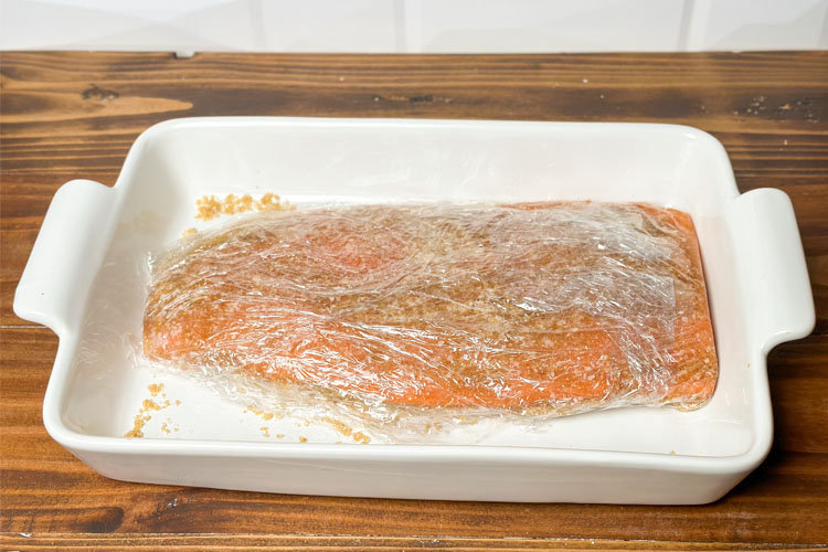 salmon filet wrapped in plastic wrap in a white dish