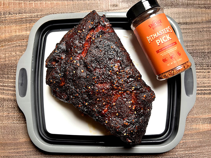 cooked pork butt next to a bottle of rub