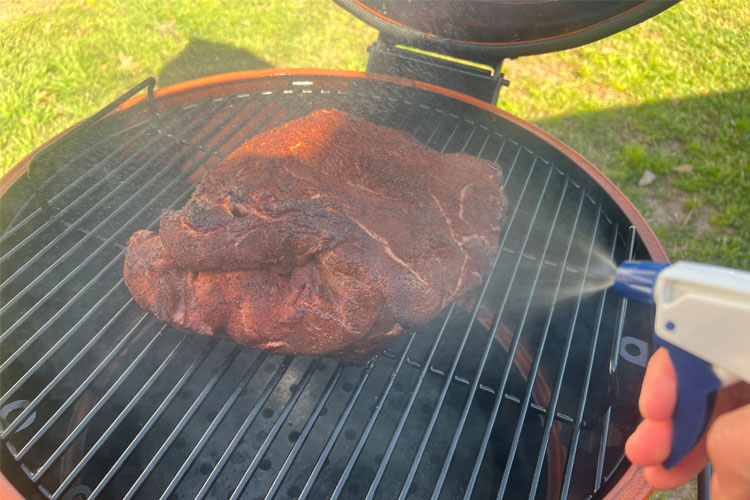 pork butt on smoker being spritzed with apple juice