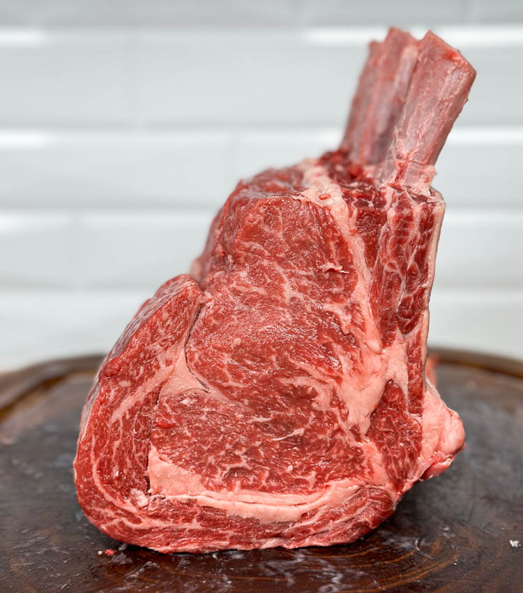 raw prime rib standing up on wooden chopping board