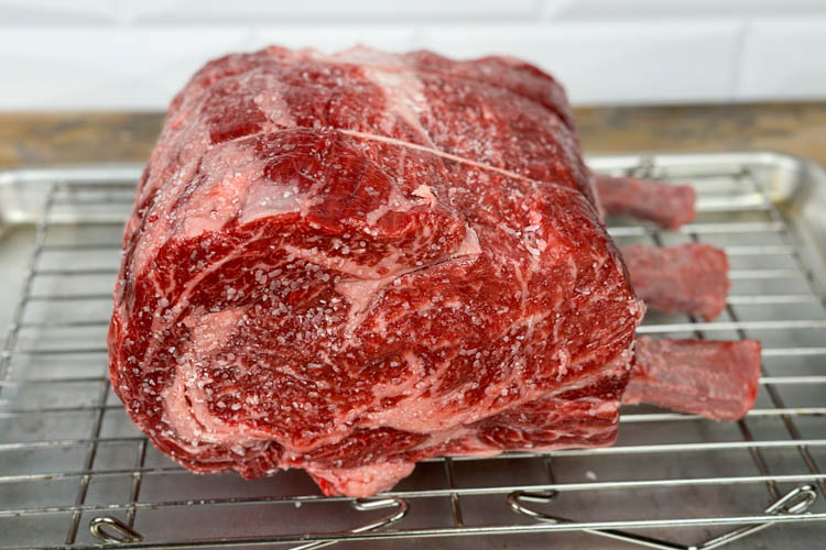 raw seasoned prime rib on a wire rack 