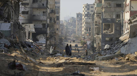 Palestinians walk between the remains of destroyed buildings following the Israeli bombardment on the main road of Gaza City on Tuesday, January 2, 2024