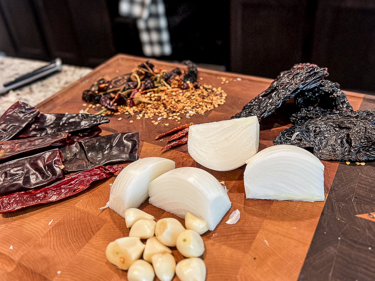 chili peppers, onions and garlic on a wooden chopping board