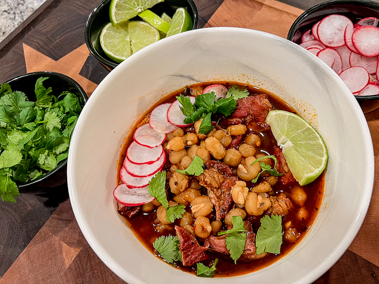 smoked pozole rojo in a white bowl with condiments