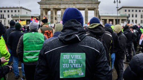 A demonstrator wears a sticker on his jacket reading: "Too much is too much" in front of Berlin's landmark Brandenburg Gate during a protest of farmers and truck drivers, on January 15, 2024 in Berlin.