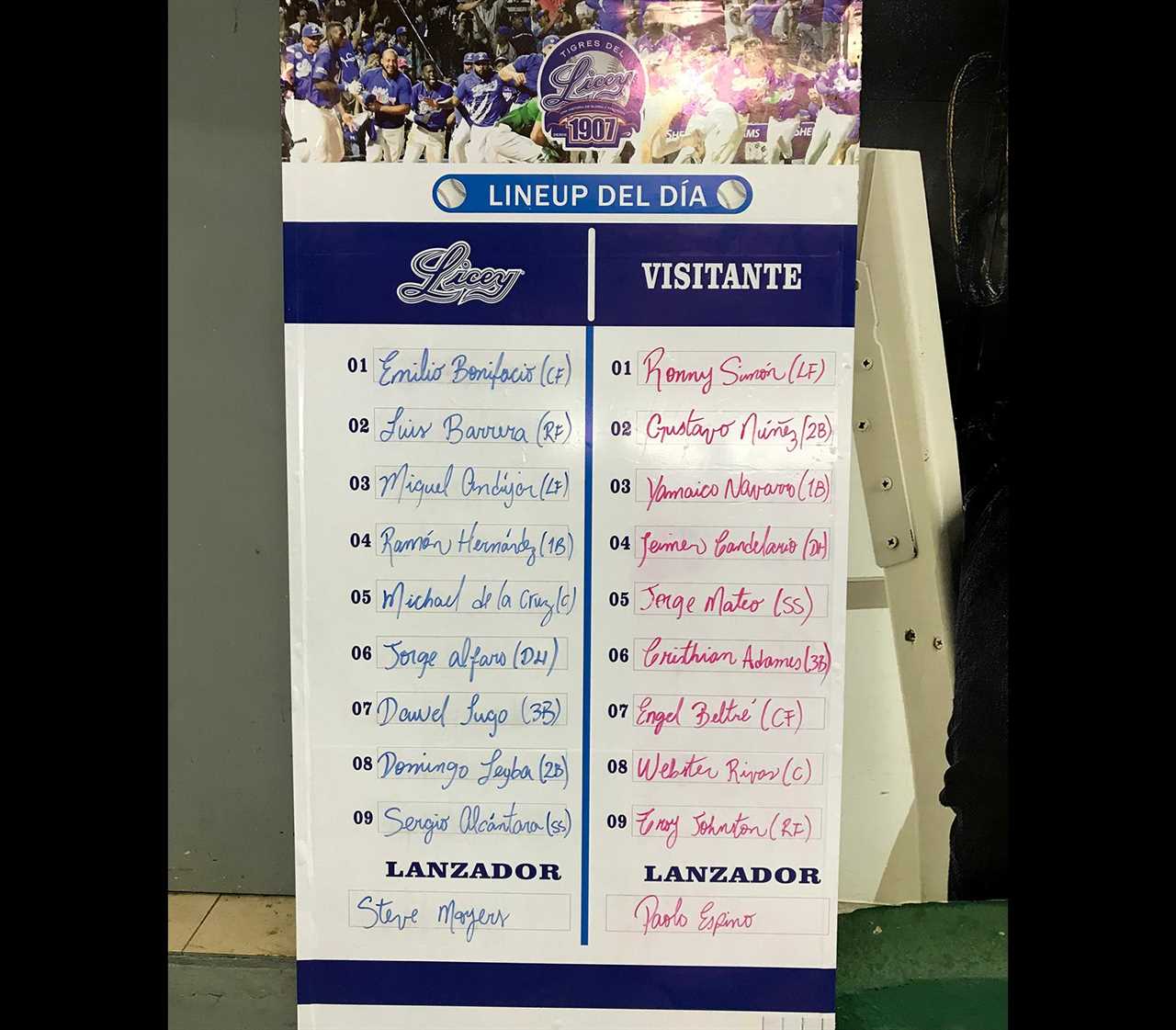 A Licey-branded sign that lists the lineups. For Licey: 01 (Emilio Bonifacio (CF) 02 Luis Barrera (RF) 03 Miguel Andújar (LF) 04 Ramón Hernández (1B) 05 Michael de la Cruz (C) 06 Jorge Alfaro (DH) 07 Davel Lugo (3B) 08 Domingo Leyba (2B) 09 Sergio Alcántara Lanzador: Steve Moyers For Visitante: 01 Ronny Simón (LF) 02 Gustavo Núñez (2B) 03 Yamaico Navarro (1B) 04 Jeimer Candelario (DH) 05 Jorge Mateo (SS) Cristhian Adames (3B) 07 Engel Beltré (CF) Webster Rivas (C) 09 Troy Johnston (RF) Lanzador: Paolo Espino