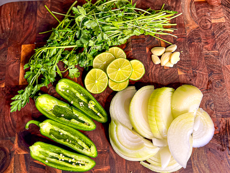 onions, jalapenos, lime slices, garlic cloves, herbs on a wooden chopping board