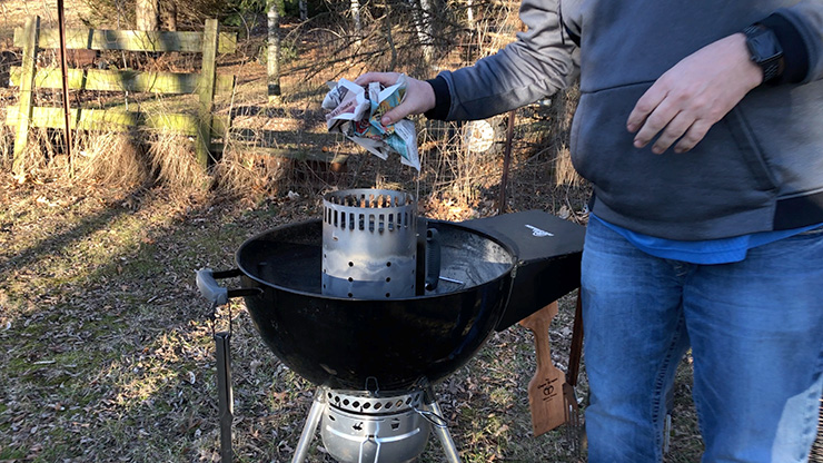 a person sticking paper to the bottom of the charcoal chimney starter