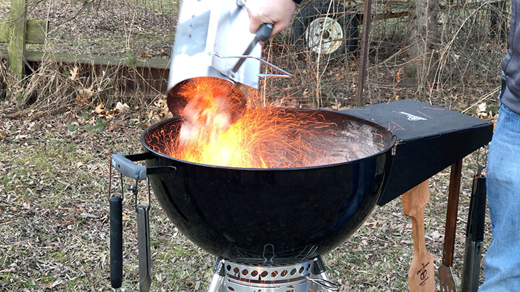 a person dumping hot charcoals from a chimney starter into a kettle grill