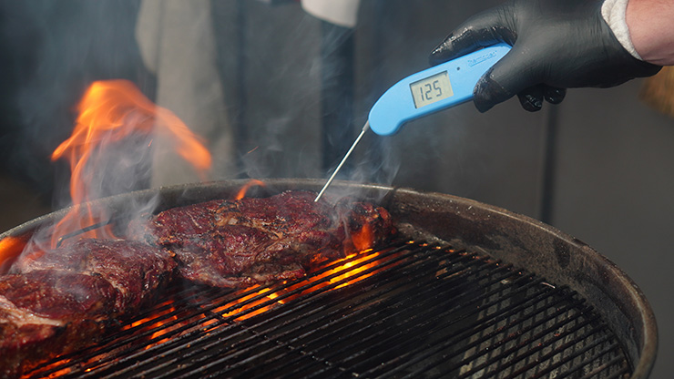 a steak with an instant read thermometer inside over a direct heat zone on a charcoal grill