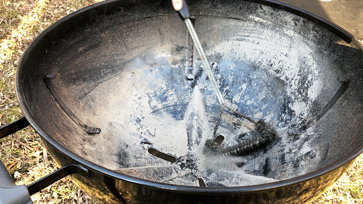 wire brush cleaning ash inside a charcoal kettle grill