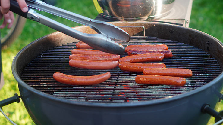 a person holding tongs over a kettle grill