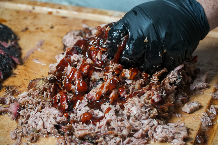 mixing the sauce into the brisket with a black gloved hand