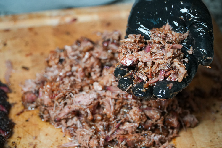 a black gloved hand holding sauced chopped brisket