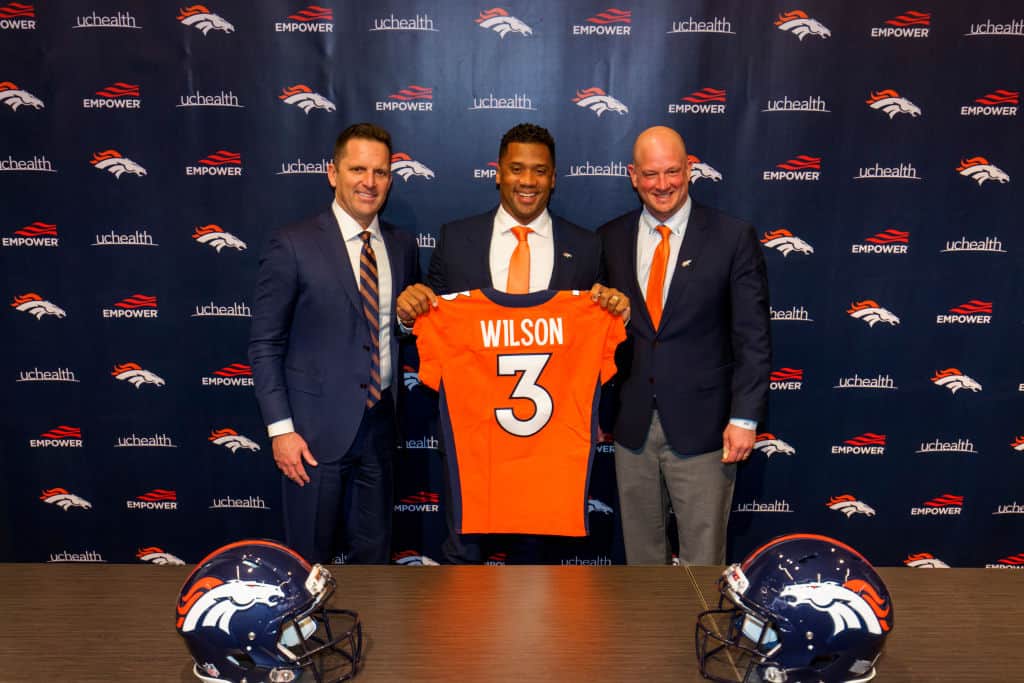 Quarterback Russell Wilson #3 of the Denver Broncos poses with his jersey alongside (L) General Manager George Paton and Head Coach Nathaniel Hackett following an introductory press conference at UCHealth Training Center on March 16, 2022 in Englewood, Colorado.