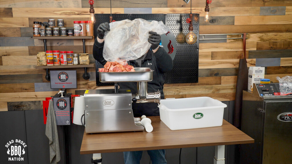 putting raw meat into the hopper of the grinder