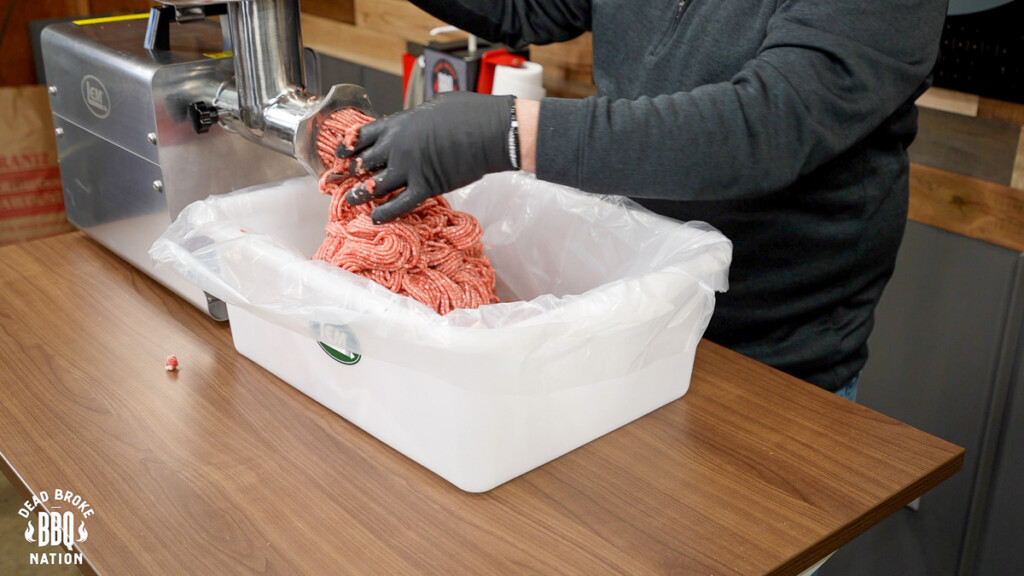 meat being extruded for the second time through the grinder into a white tub
