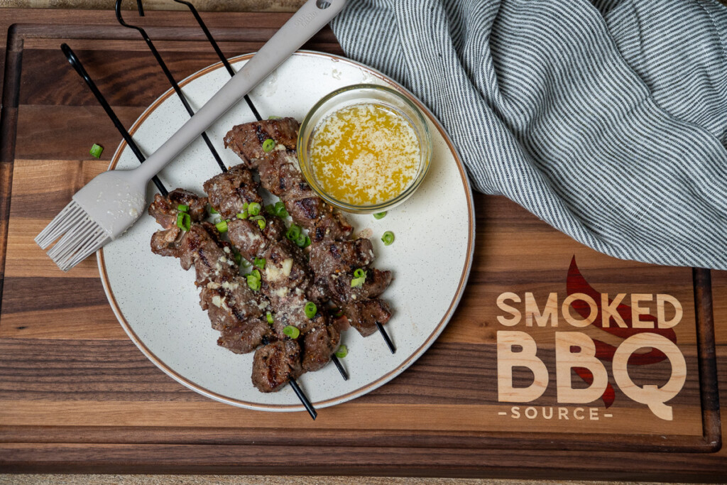 grilled steak bites skewers on a white plate with a bowl of butter garlic parmesan sauce