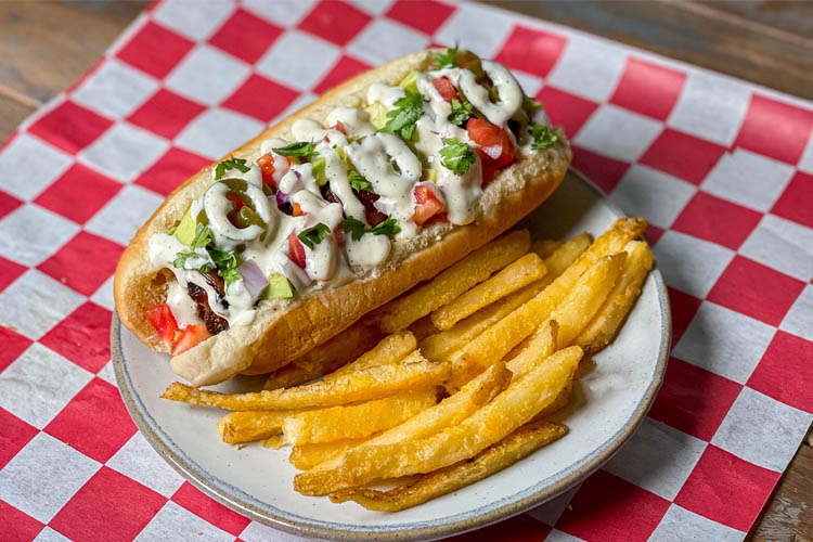 sonoran hotdot and fries on a white plate sitting on a red and white check napkin