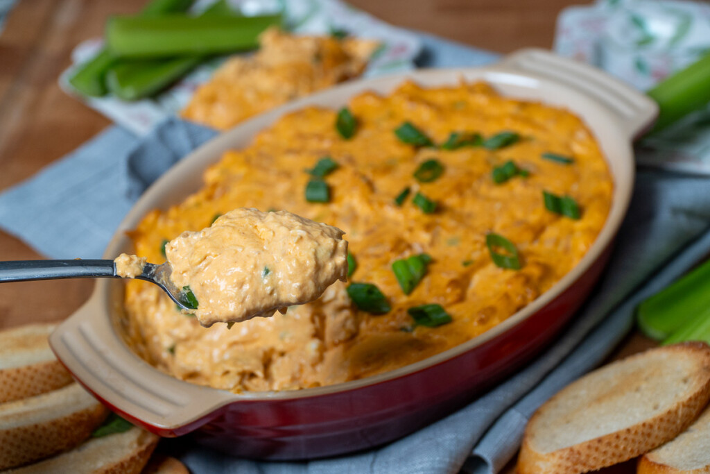 a spoonfull of buffalo chicken dip in front of a dish of buffalo chicken dip