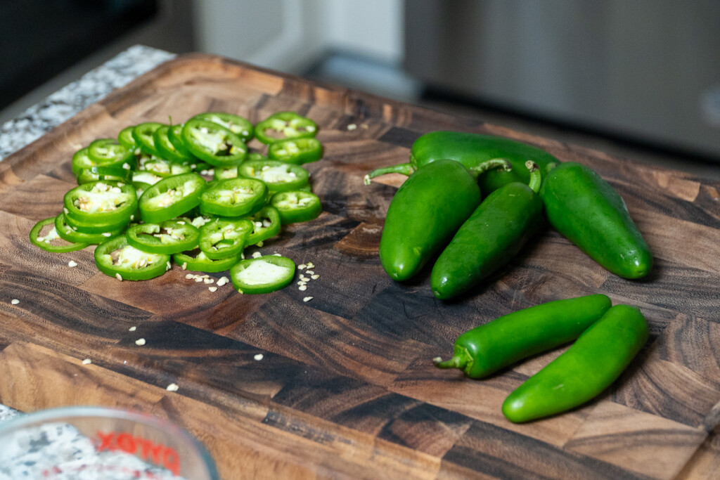 whole and sliced jalapenos on a wooden board