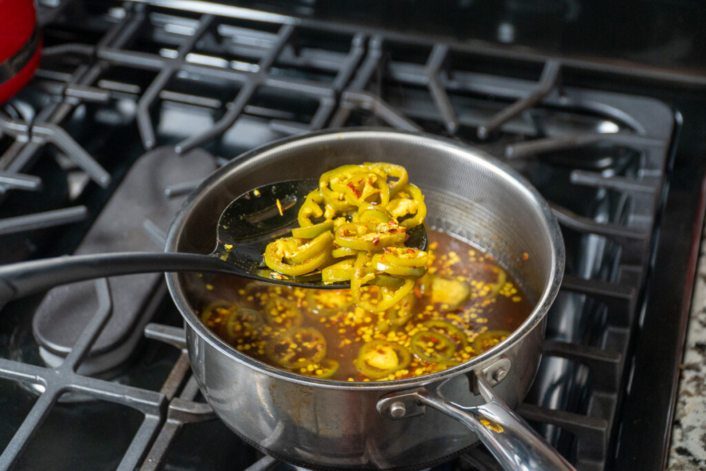 a spoon lifting jalapenos out of a pot of liquid