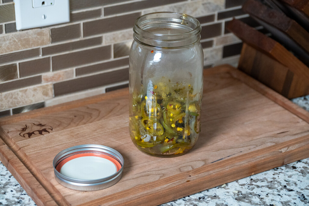 a half full jar of cooked jalapenos on a wooden board